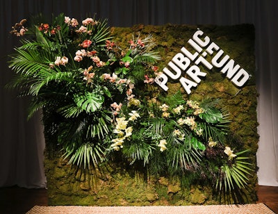The step-and-repeat photo backdrop featured lush greenery and a moss-covered wall.